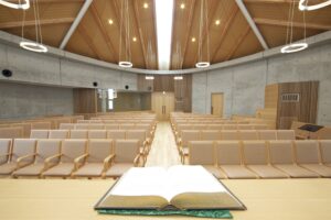 開かれた聖書の向こうに木製の椅子が並ぶ、明るく落ち着いた教会礼拝堂の内部